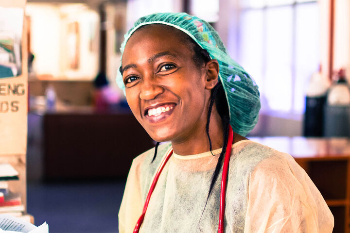 Smiling medical personnel wearing surgical gown and cap.